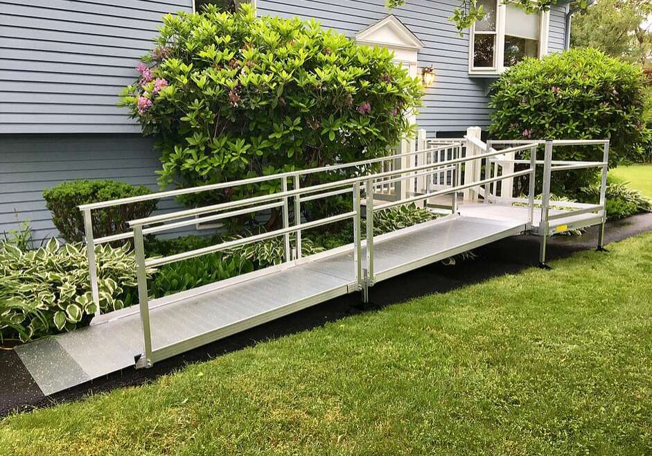 Metal wheelchair ramp at the entrance of a blue house with a grass lawn. 